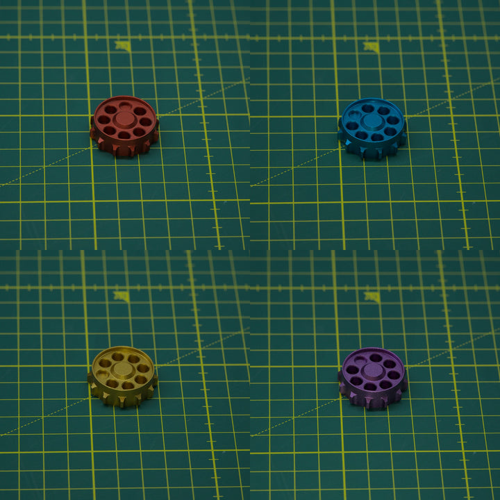 Four small circular metal components in red, blue, gold, and purple are arranged on a green gridded cutting mat background.