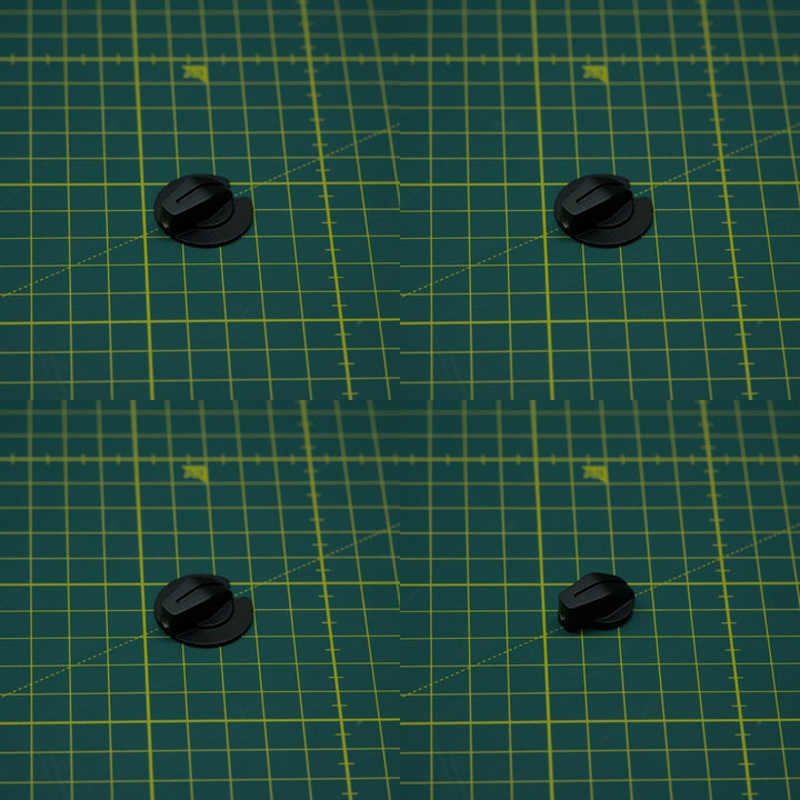 Four small black plastic toggle knobs arranged in a 2x2 grid on a green cutting mat with yellow grid lines.